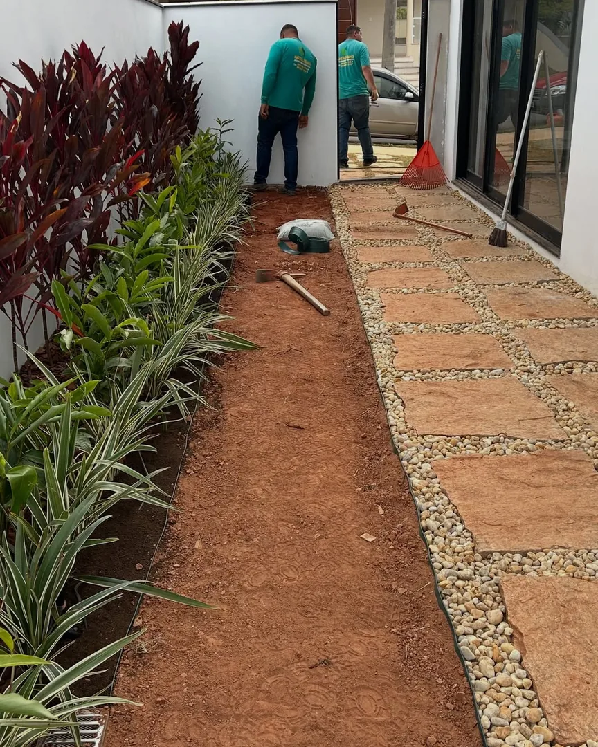 Equipe executando caminho pavimentado com pedras e bordadura de seixo, junto a canteiro de cordyline